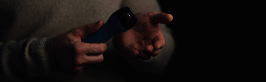częściowy widok człowieka trzymającego latarkę elektryczną podczas przerwy w zasilaniu izolowany na czarno, baner - Zdjęcie, obraz