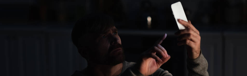 huolestunut mies osoittaa älypuhelimeen samalla kiinni kadonnut signaali sähkökatkoksen aikana, banneri - Valokuva, kuva