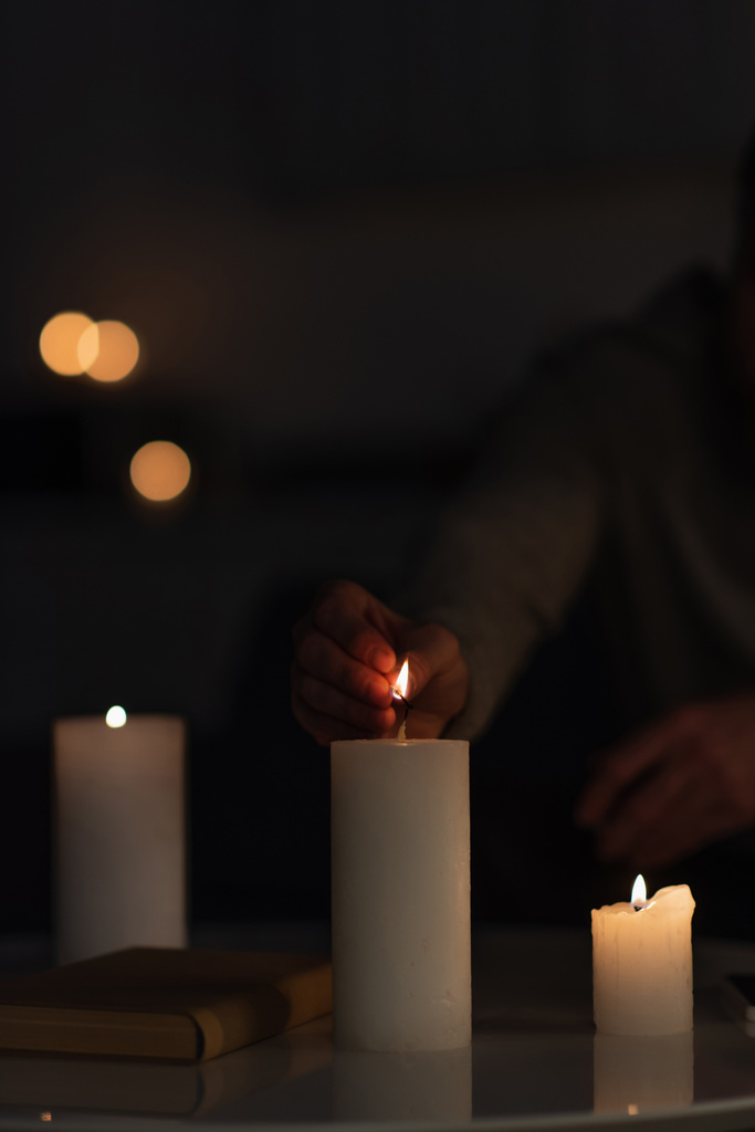 abgeschnittene Ansicht eines Mannes, der Kerzen in der Dunkelheit anzündet, verursacht durch Stromausfall - Foto, Bild