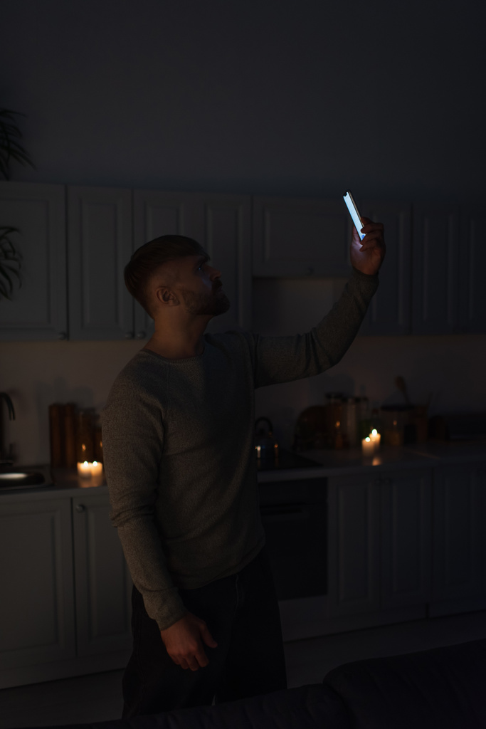 hombre sosteniendo el teléfono celular en la mano levantada mientras capta la señal durante el corte de energía - Foto, Imagen