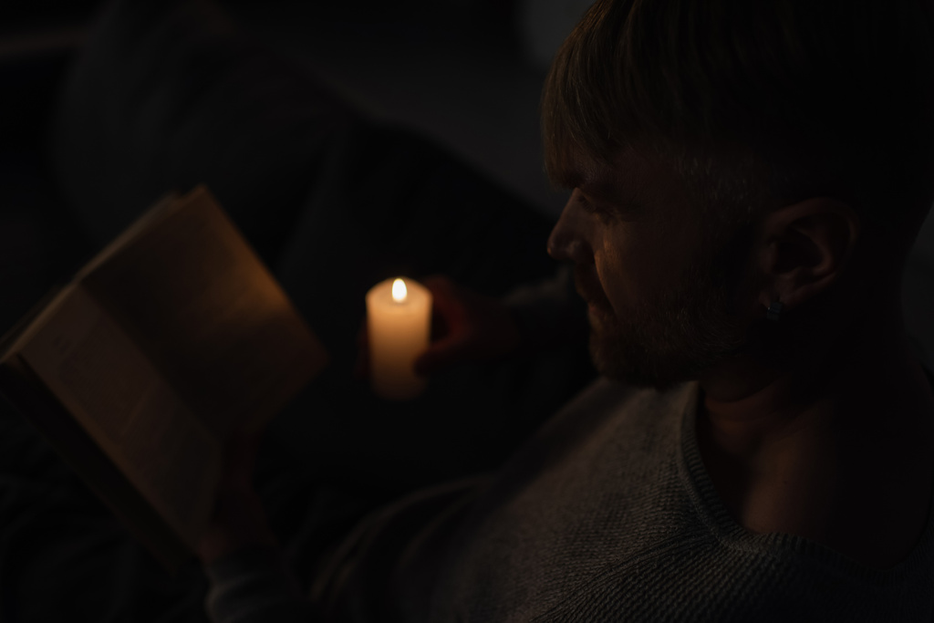 uomo che tiene accesa la candela mentre legge il libro nell'oscurità causata dal blackout energetico - Foto, immagini