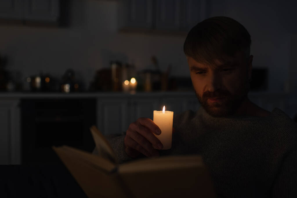 людина тримає запалену свічку під час читання книги на темній кухні під час вимкнення електрики
 - Фото, зображення