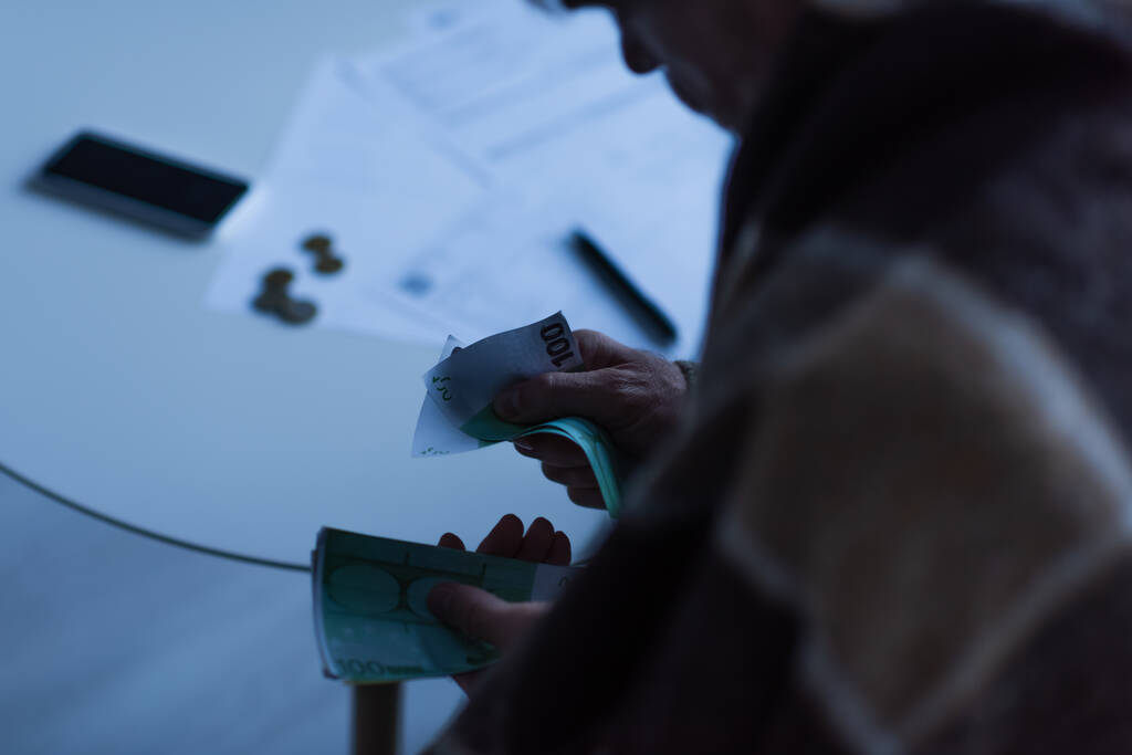 vue recadrée de l'homme comptant l'argent près des factures floues pendant la panne d'électricité - Photo, image