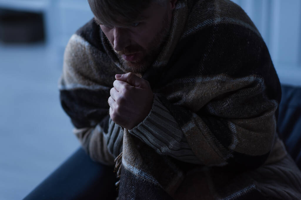 homem congelado sentado em cobertor quente e mãos quentes durante o desligamento da eletricidade em casa - Foto, Imagem
