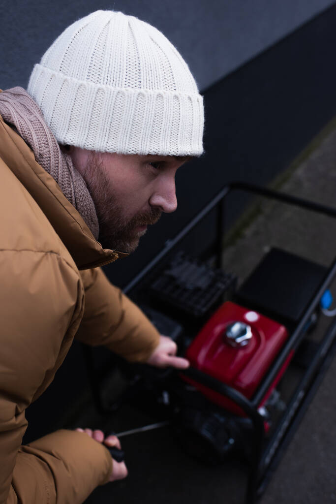 uomo in maglia cappello guardando lontano mentre si avvia generatore di potenza su sfondo sfocato - Foto, immagini