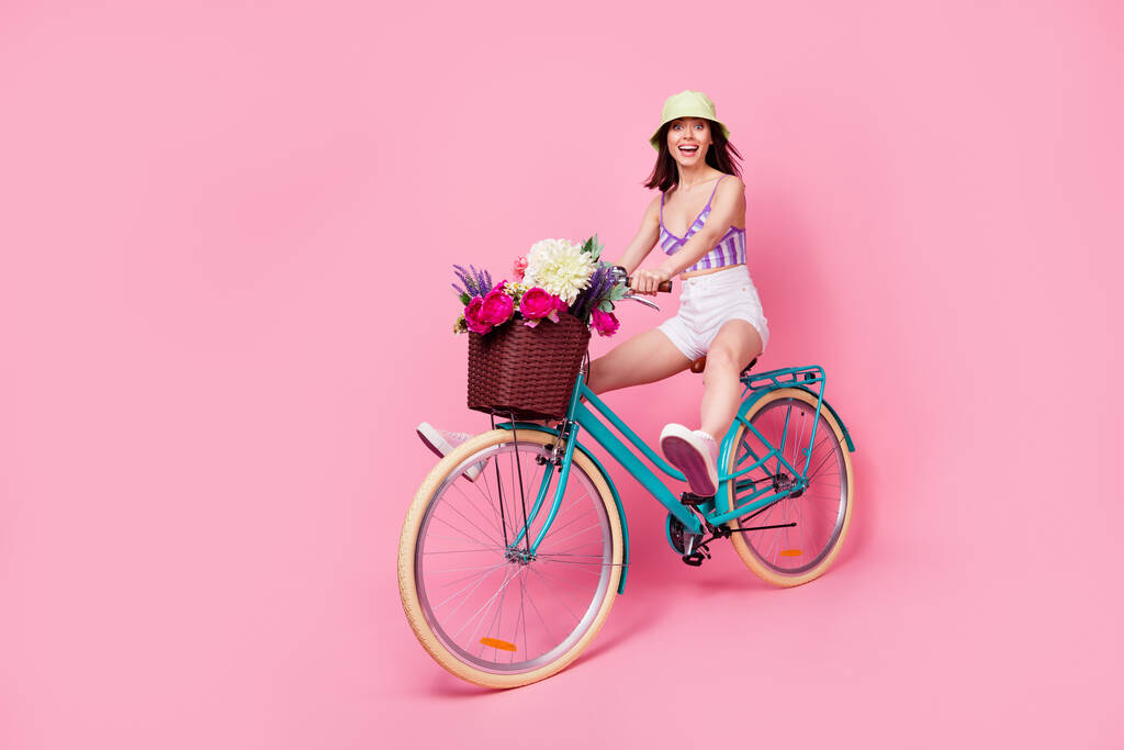 Foto de longitud completa de excitada chica funky vestido violeta superior que se divierte conduciendo bicicleta espacio vacío aislado color rosa fondo. - Foto, imagen