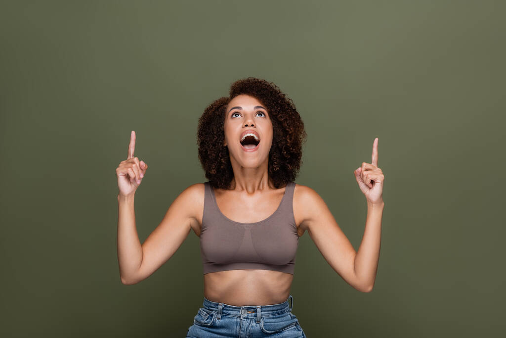Excited african american woman in top pointing with fingers up isolated on green  - Photo, Image