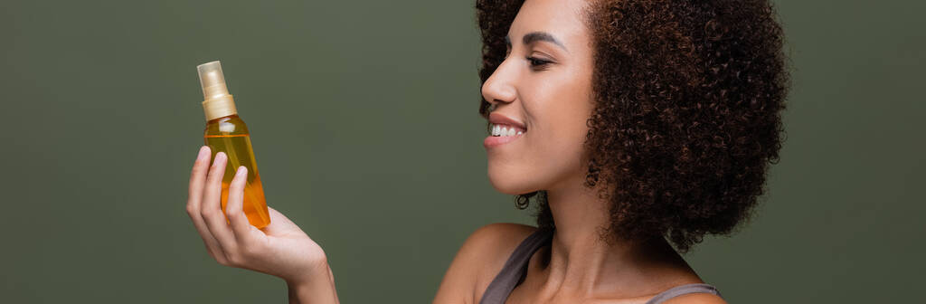 緑、バナーに隔離された化粧品油を見ているアフリカ系アメリカ人女性の側面図  - 写真・画像