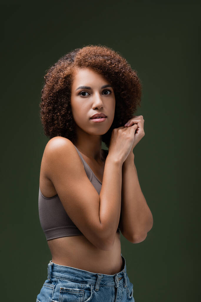 Porträt einer lockigen Afroamerikanerin in Top, die isoliert auf dunkelgrün in die Kamera blickt  - Foto, Bild