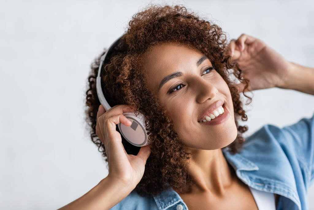 ワイヤレスヘッドフォンで音楽を聴きながら笑う幸せなアフリカ系アメリカ人女性  - 写真・画像