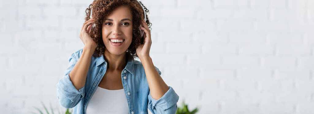 mulher afro-americana positiva sorrindo enquanto ouve música em fones de ouvido sem fio, banner  - Foto, Imagem