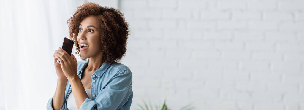 izgatott afro-amerikai nő gazdaság smartphone üres képernyőn, és néz félre, banner - Fotó, kép