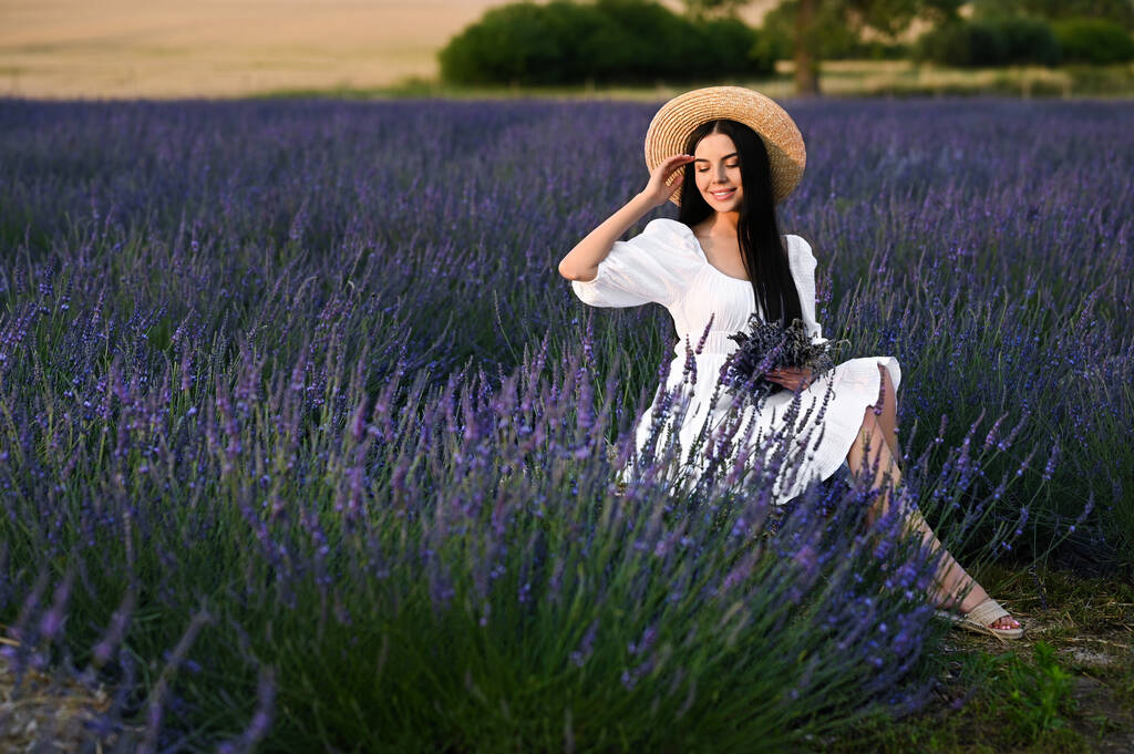 Beautiful young woman with bouquet sitting in lavender field - Fotografie, Obrázek