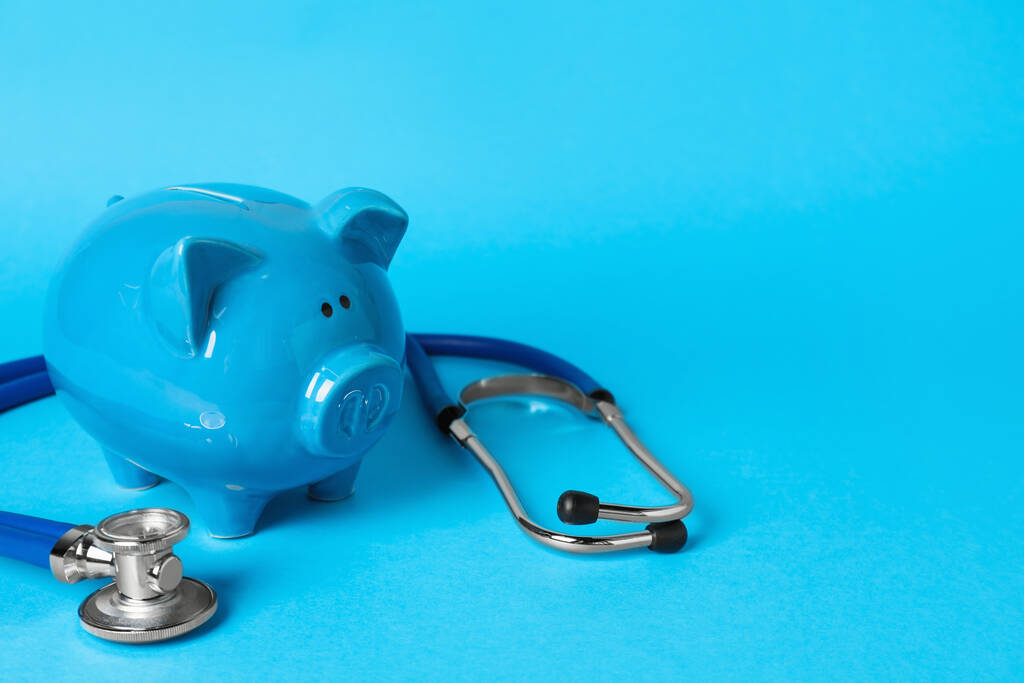 Keramisches Sparschwein und Stethoskop auf hellblauem Hintergrund, Platz für Text. Krankenversicherung - Foto, Bild