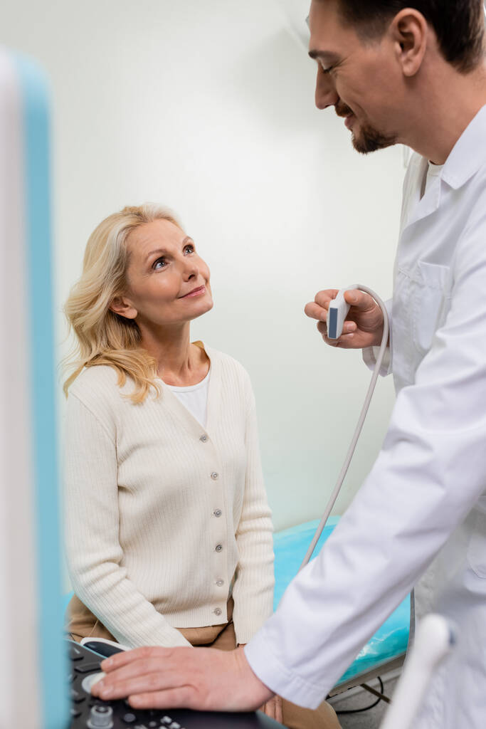 szczęśliwy lekarz z sondą ultrasonograficzną patrząc na szczęśliwą blondynkę w szpitalu - Zdjęcie, obraz