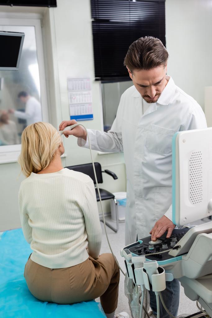 lékař v bílém plášti upravující ultrazvuk při diagnostice ženy středního věku - Fotografie, Obrázek