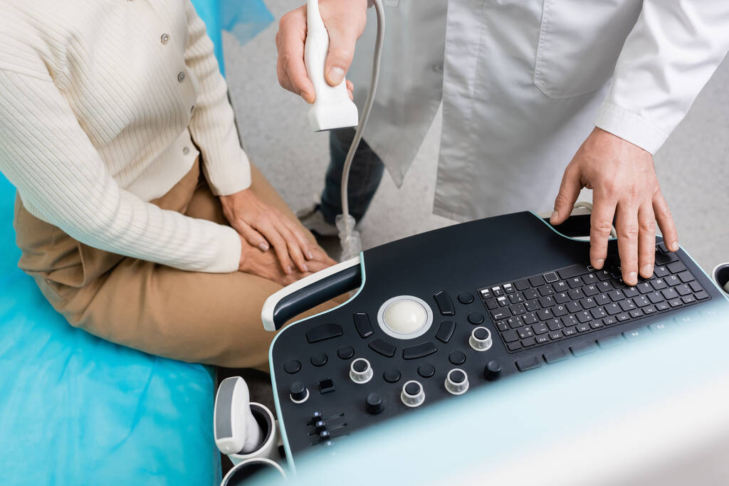 vista recortada del médico que sostiene la sonda de ultrasonido cerca del panel de control y la mujer en la clínica - Foto, Imagen