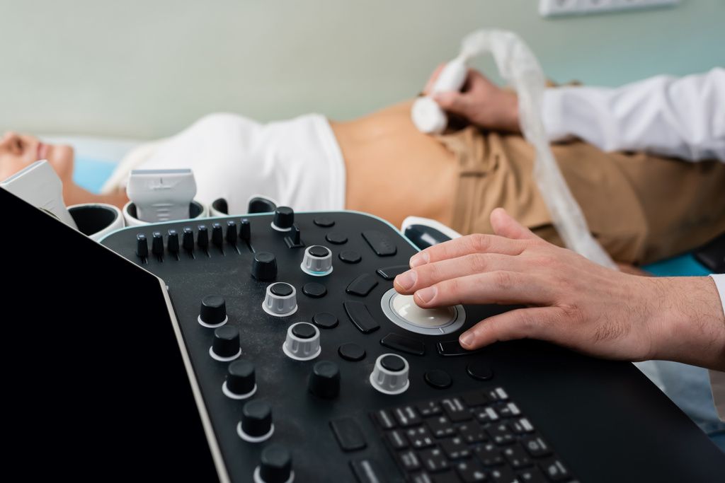 vue partielle du médecin opérant une machine à ultrasons tout en effectuant un examen abdominal de la femme floue - Photo, image