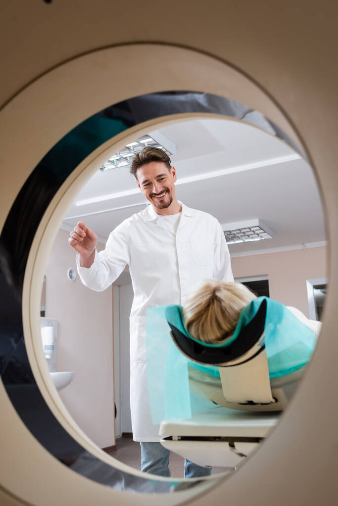 positiver Radiologe lächelt Patient vor Computertomographie an - Foto, Bild
