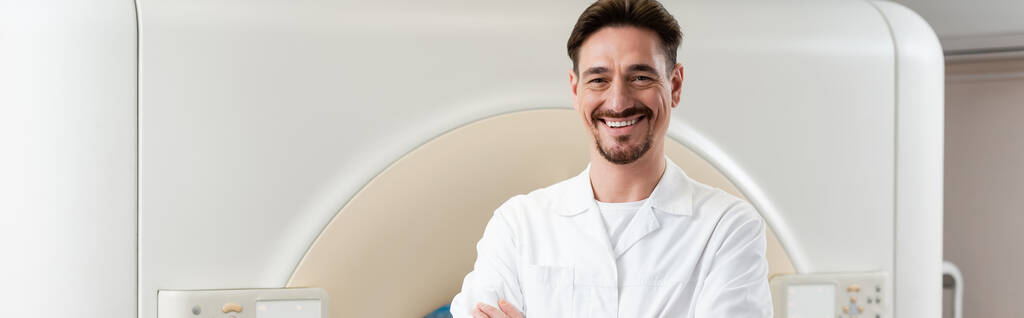 alegre médico sonriendo a la cámara mientras está de pie cerca del escáner de tomografía computarizada, pancarta - Foto, imagen