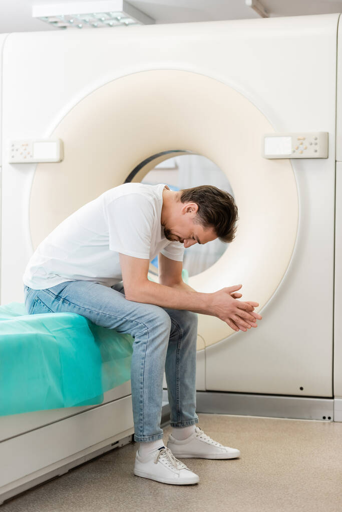 повна довжина депресивного чоловіка, що сидить з похилою головою біля комп'ютерної томографічної машини
 - Фото, зображення
