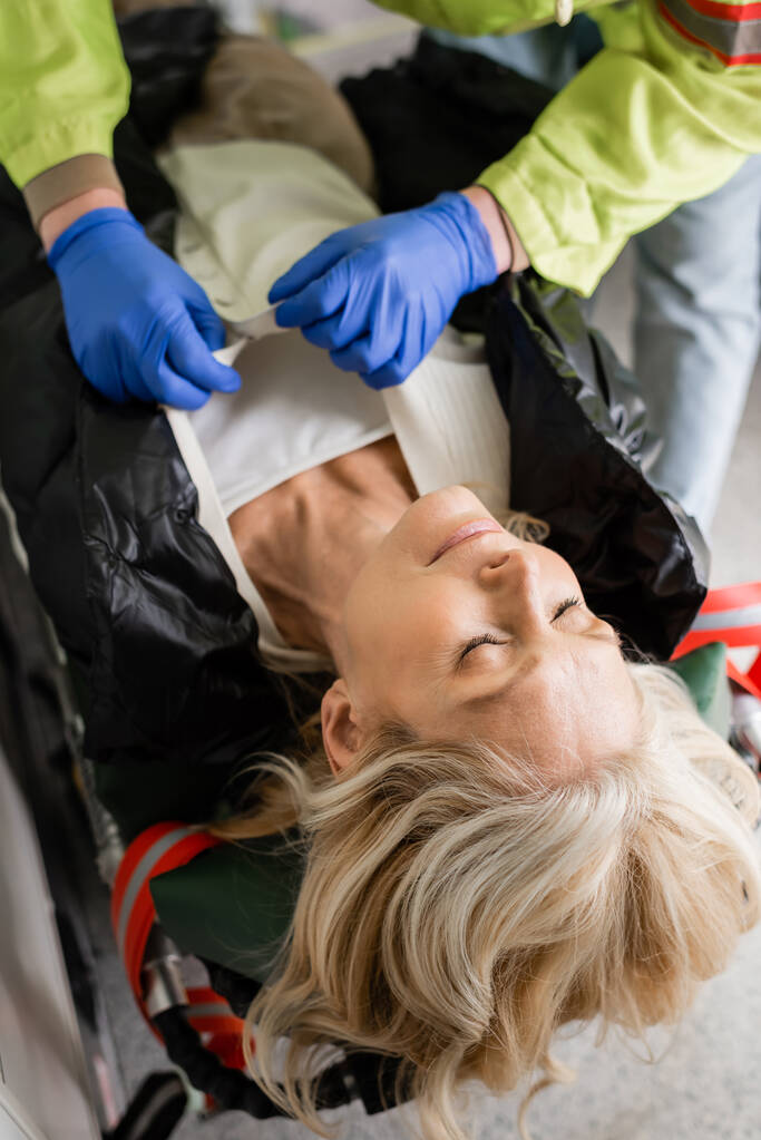 Ensihoitaja riisuu vaatteita tajuttomalta kypsältä naiselta hätäajoneuvossa  - Valokuva, kuva