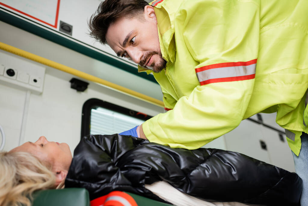 Paramédico en uniforme dando primeros auxilios al paciente inconsciente en vehículo de emergencia  - Foto, Imagen