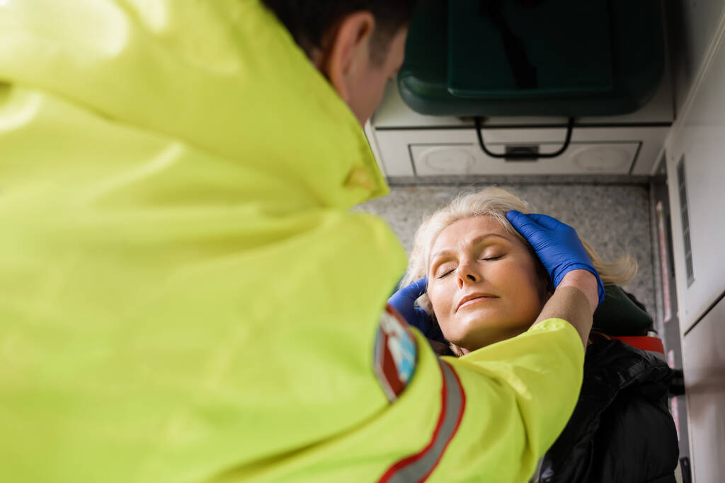 Высокий угол обзора размытого парамедика, проверяющего зрелого пациента в машине скорой помощи  - Фото, изображение