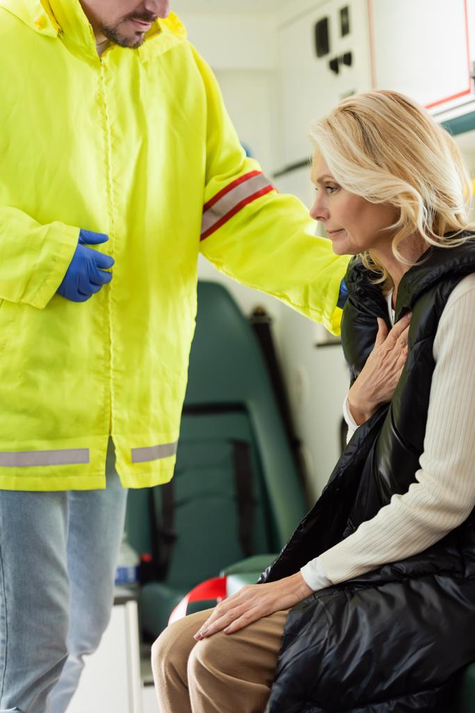 Парамедик в форме, успокаивает взрослую женщину в машине скорой помощи  - Фото, изображение