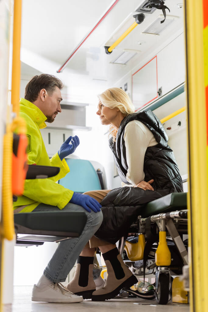 Sivukuva ensihoitajasta lateksikäsineissä puhumassa kypsälle potilaalle hätäautossa  - Valokuva, kuva
