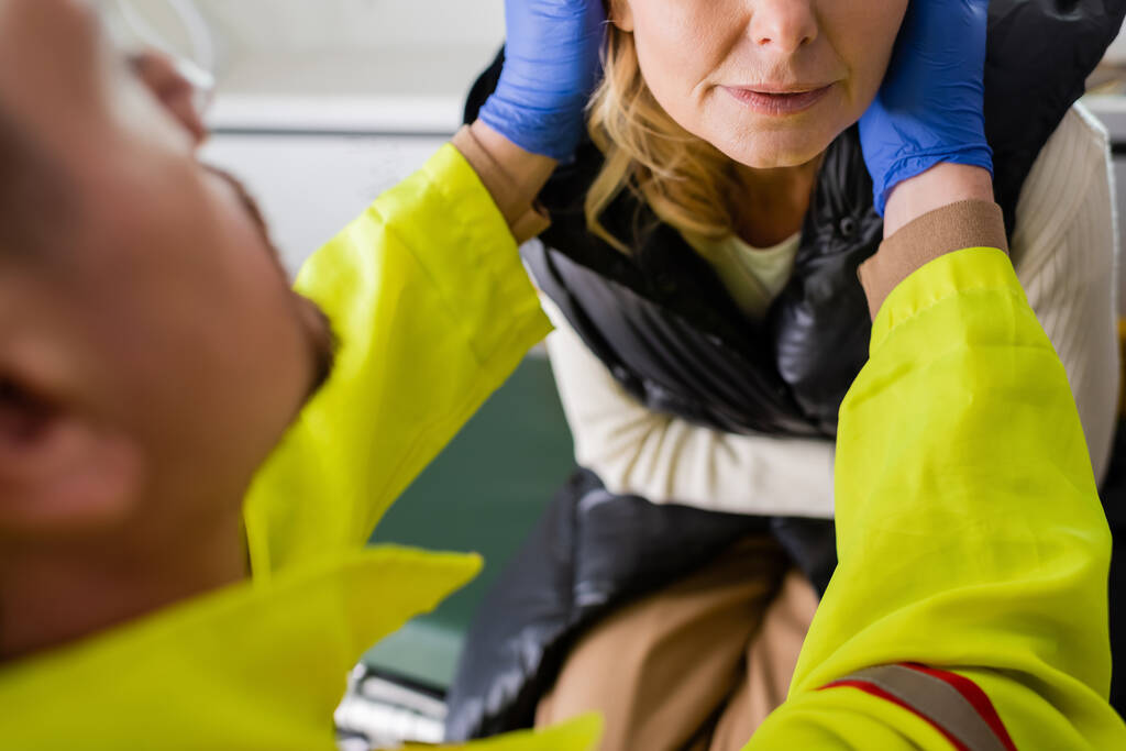 Vista cortada de paramédico desfocado em luvas de látex dando primeiros socorros para mulher de meia-idade  - Foto, Imagem