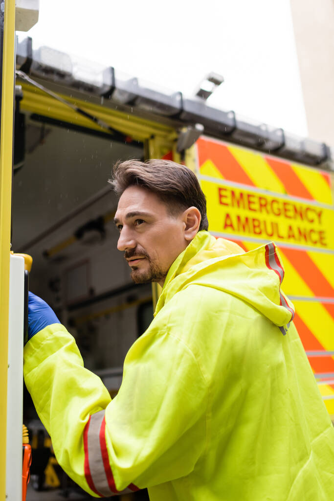 Paramedicus in uniform openen deur van ambulance auto op straat  - Foto, afbeelding