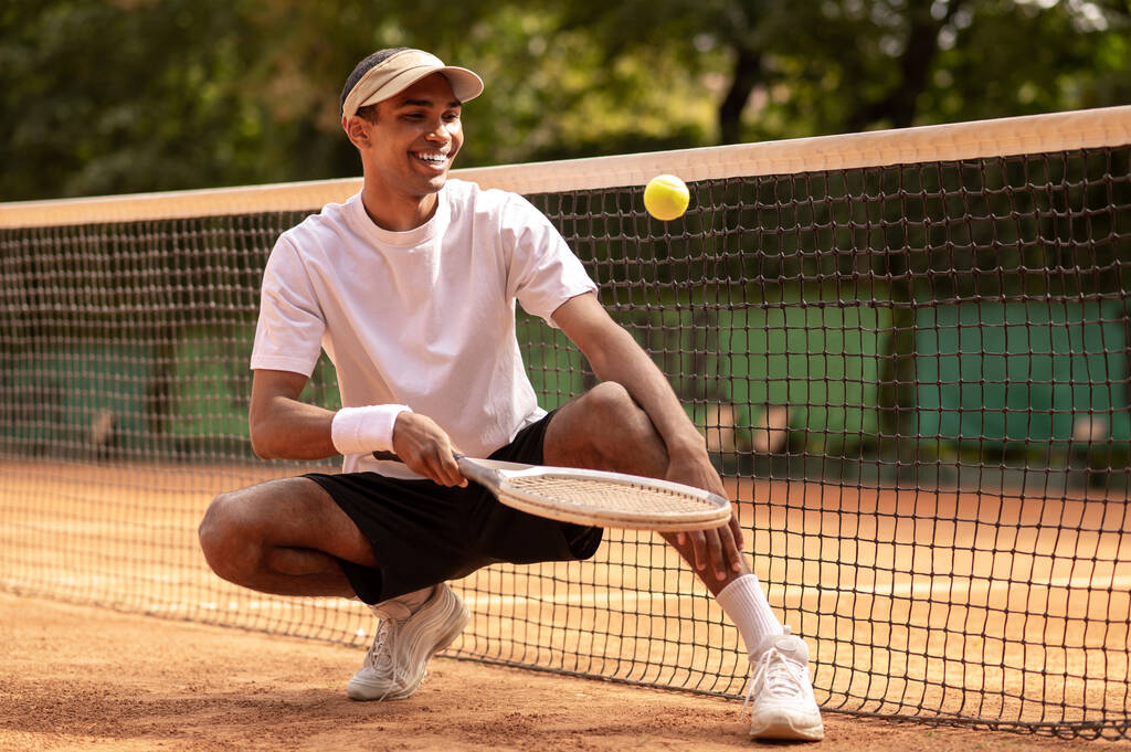 Sportliche Zeit. Junger Mann in weißem T-Shirt und Sonnenbrille auf den Tennisplätzen - Foto, Bild