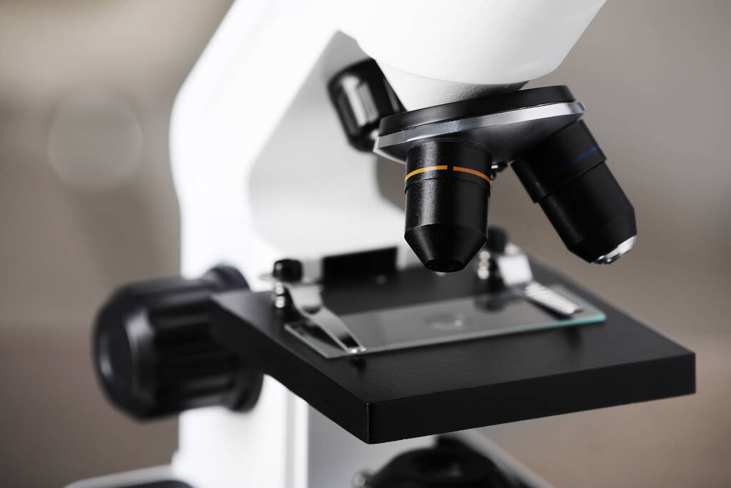 Nowoczesny mikroskop medyczny ze szklanym szkiełkiem na rozmytym tle, zbliżenie. Sprzęt laboratoryjny - Zdjęcie, obraz