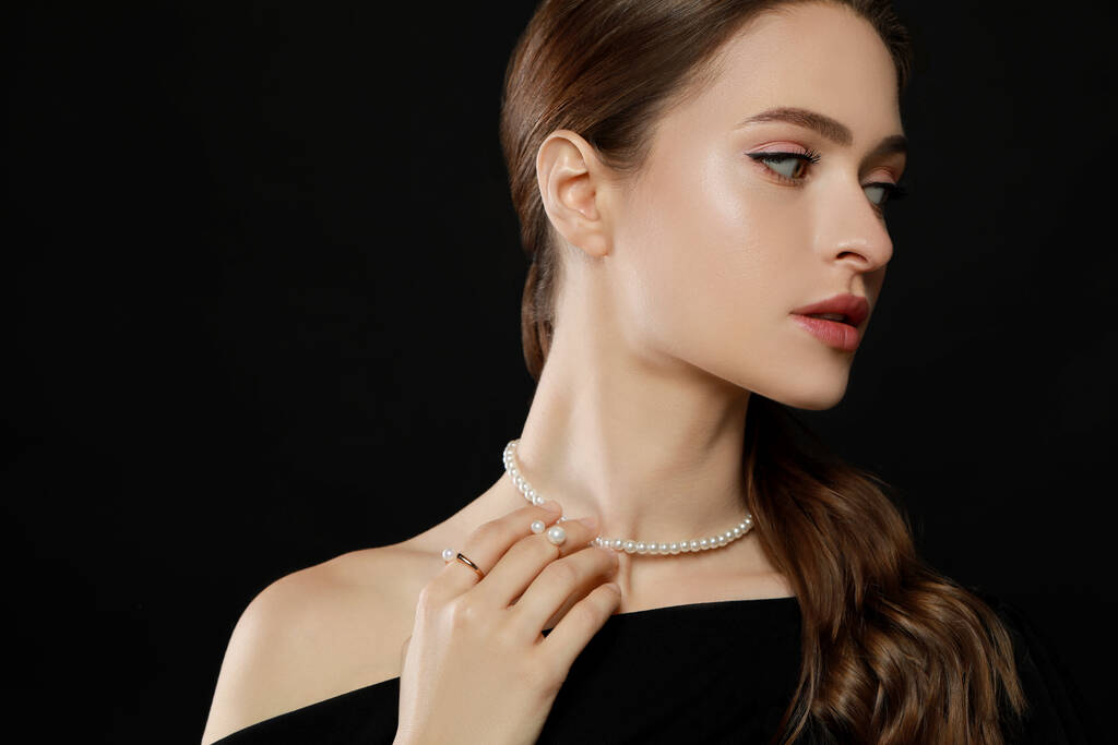 Mujer joven con elegantes joyas de perlas sobre fondo negro, espacio para el texto - Foto, Imagen