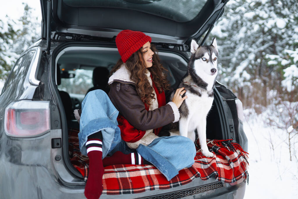 Νεαρή γυναίκα και χαριτωμένο σκυλί husky απολαμβάνοντας σε εξωτερικούς χώρους στο αυτοκίνητο. Ταξιδιωτική ιδέα. Χειμερινή περίοδος. - Φωτογραφία, εικόνα