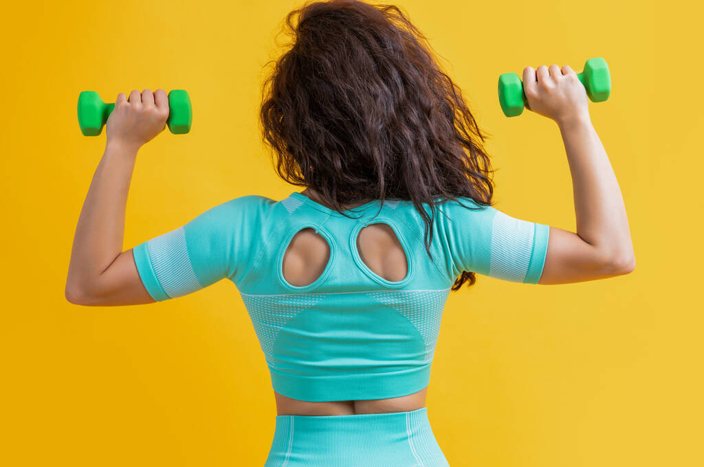 Fitness-Frau macht Gewichtheben mit Kurzhantel, Rückenansicht. Fitness-Frau macht Gewichtheben Übung isoliert auf gelbem Hintergrund. Fitness und Sport. - Foto, Bild