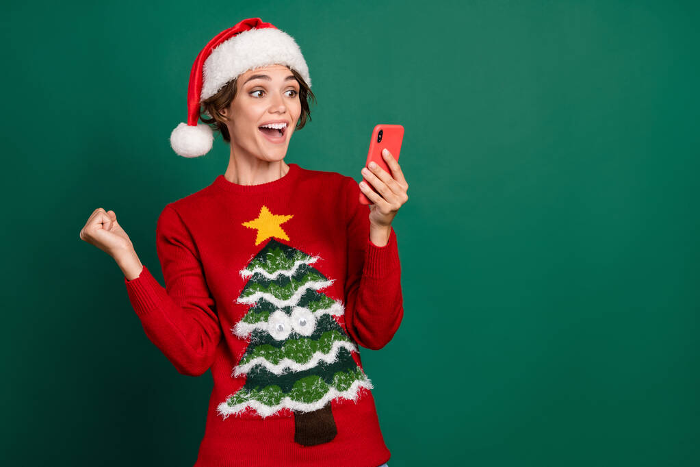 Foto van opgetogen persoon verhogen vuist vieren succes houden telefoon geïsoleerd op groene kleur achtergrond. - Foto, afbeelding