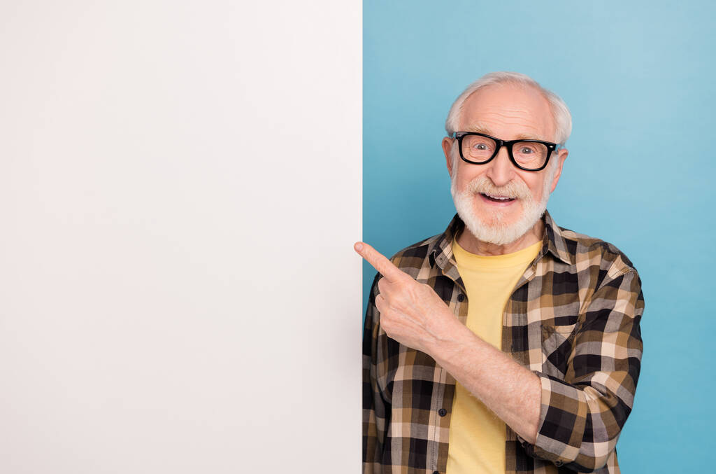 Photo de l'homme retraité assez confiant porter des lunettes chemise à carreaux pointant placard espace vide isolé fond de couleur bleue. - Photo, image