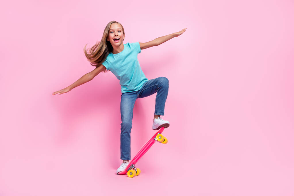 Volledige lengte foto van zoete opgewonden kleine jongen dragen turquoise t-shirt rijden skateboard lege ruimte geïsoleerde roze kleur achtergrond. - Foto, afbeelding