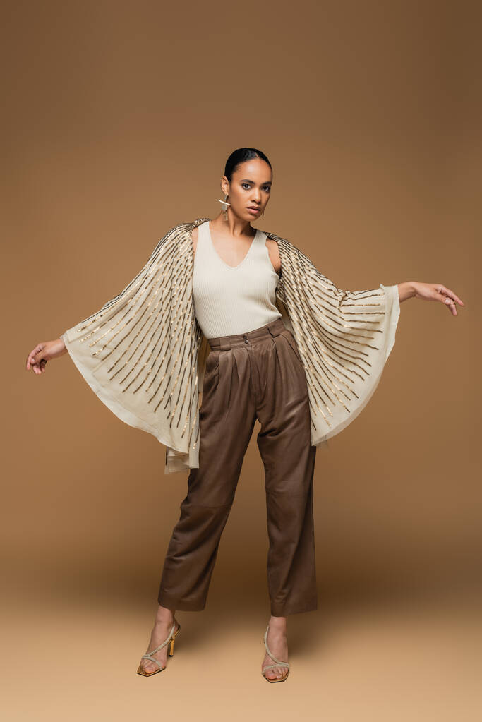 full length of stylish african american woman in golden shawl gesturing on beige - Photo, Image