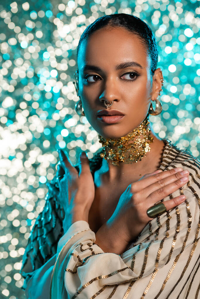 modelo afroamericano perforado con lámina de oro en el cuello posando con brazos cruzados sobre fondo azul brillante  - Foto, imagen