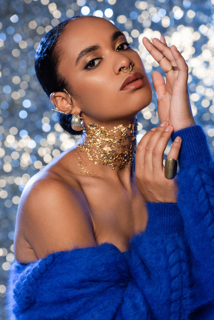Mujer afroamericana de moda en chaqueta de piel sintética azul y accesorios dorados sobre fondo brillante  - Foto, Imagen