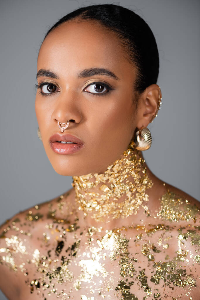 Modna Afroamerykanka ze złotymi akcesoriami i folią na klatce piersiowej odizolowana na szaro  - Zdjęcie, obraz