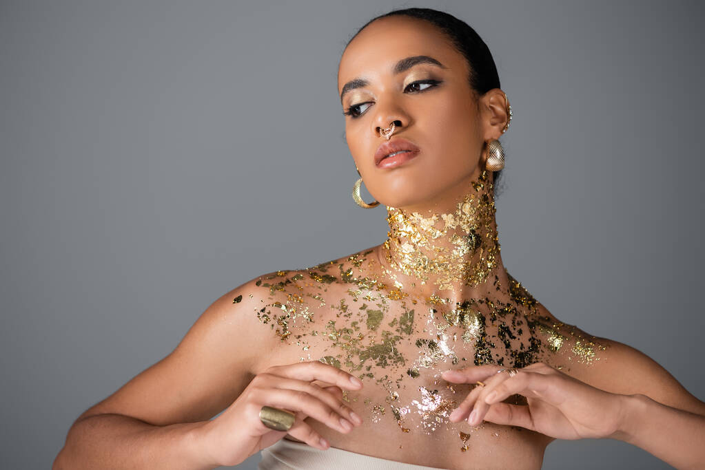 Trendikäs afrikkalainen amerikkalainen malli kultainen folio rinnassa poseeraa harmaalla  - Valokuva, kuva