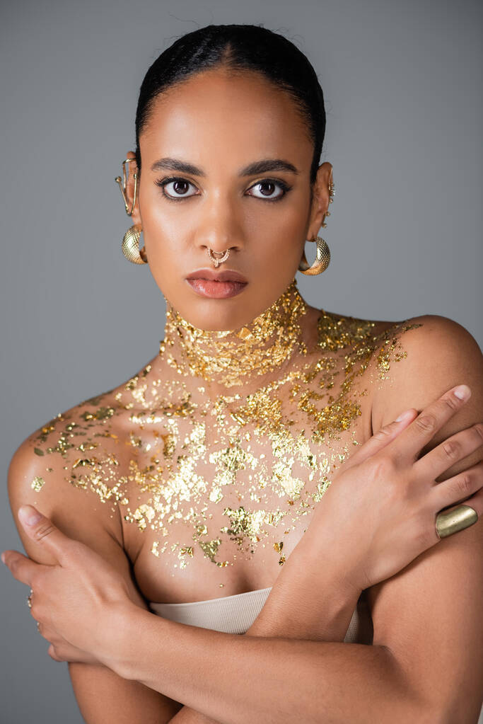 トレンディアフリカ系アメリカ人のモデルで首に金色の箔がグレーに隔離されたポーズ  - 写真・画像
