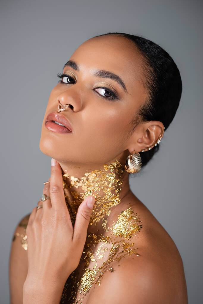 Portrait of trendy african american model touching golden foil on neck isolated on grey  - Photo, Image