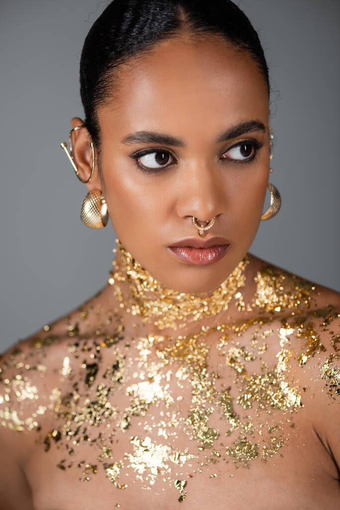 Retrato de modelo afroamericano de moda con accesorios y lámina dorada posando aislada sobre gris  - Foto, imagen