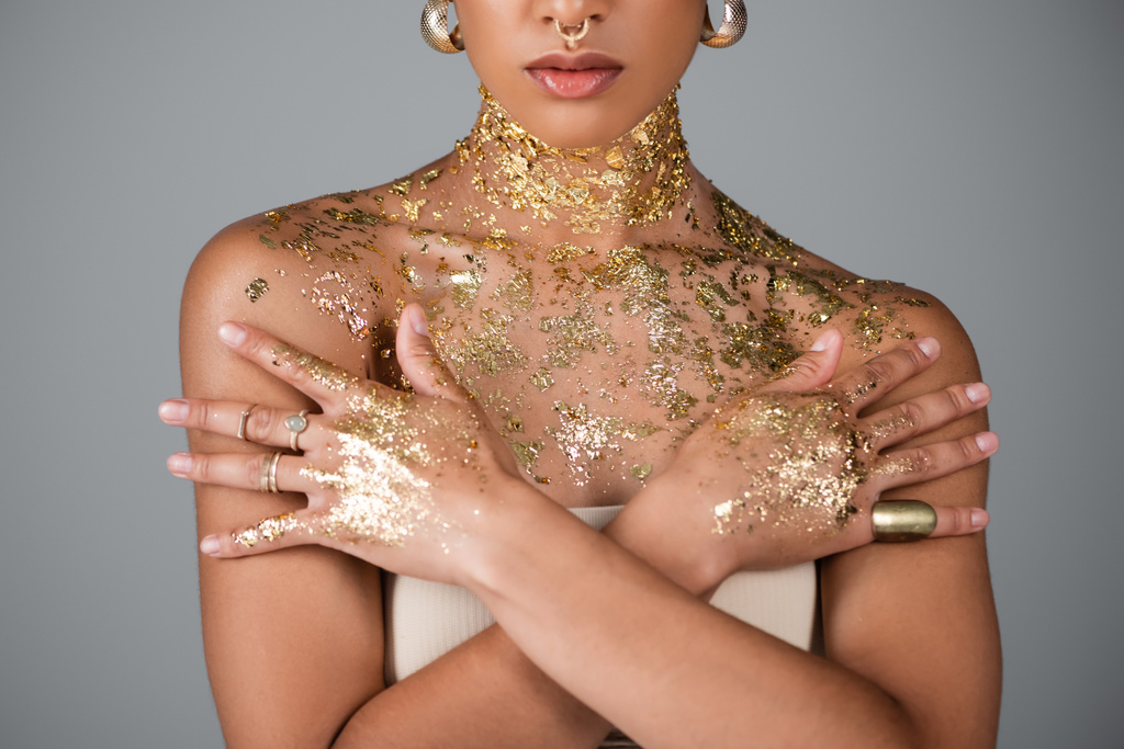 Partial view of african american model with golden foil on hands and chest posing isolated on grey  - Photo, Image