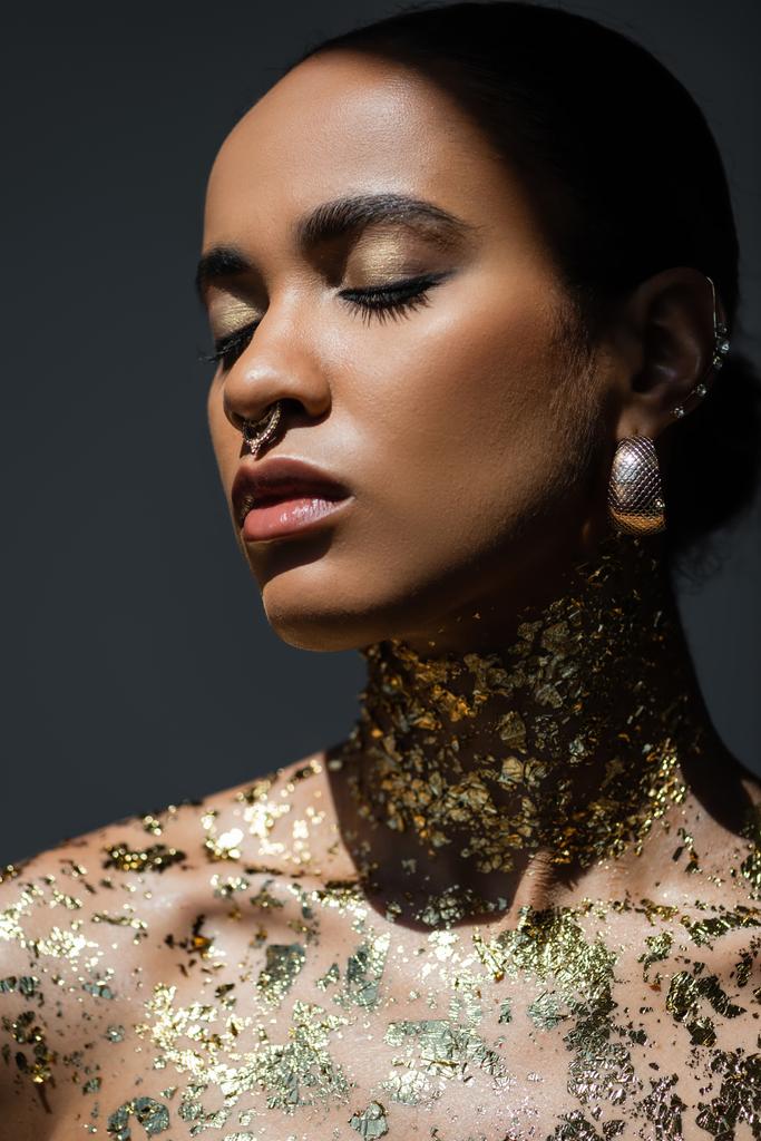 Egy fiatal afro-amerikai nő portréja, arany fóliával a testén, szürke árnyalattal elszigetelve.  - Fotó, kép
